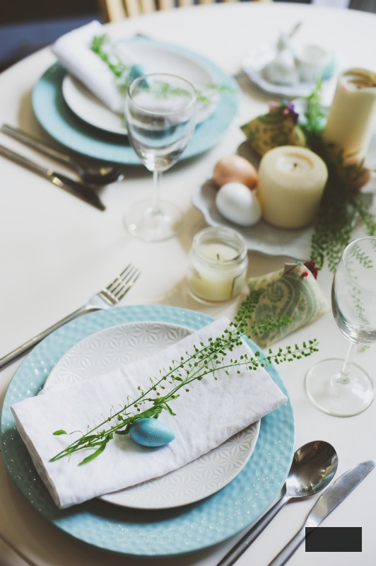 Easter and spring festive table decorated in blue and white tones in natural rustic style, with eggs, bunny, fresh flowers and candles.