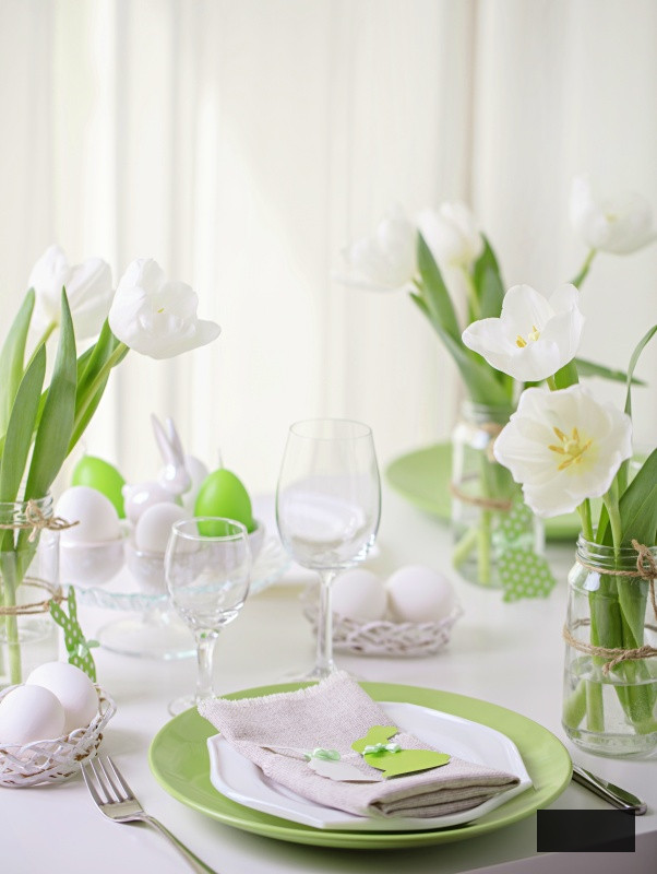 Decor and table setting of the Easter table is a vase with white tulips and dishes of green and white color. Easter decor with white polka dots.