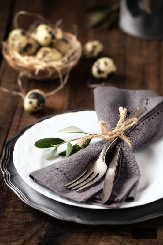 Easter table setting with vintage silverware with an olive branch on a white plate with quail eggs in a decorative nest at the background