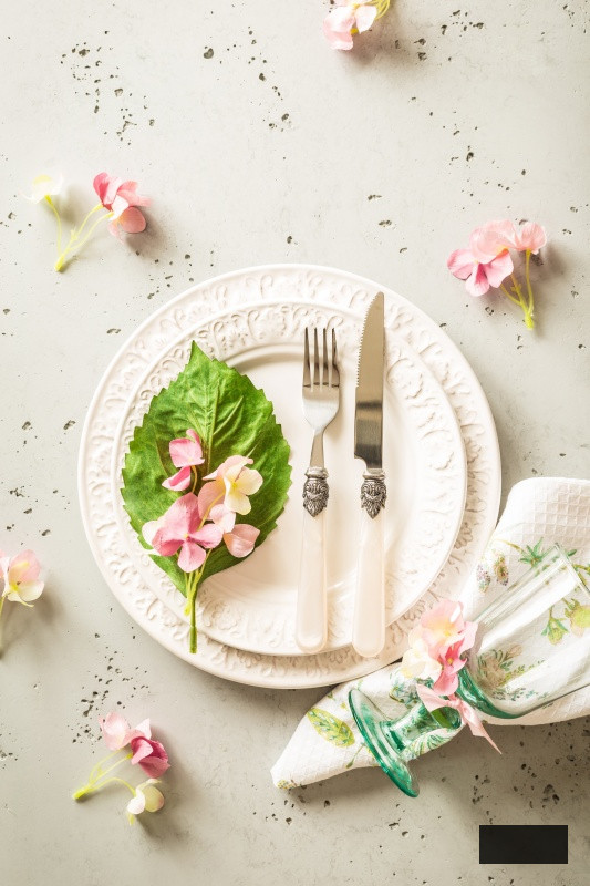Easter, spring or summer table setting design captured from above (top view, flat lay). Ornamental white plates, glass, cutlery and pink flowers.