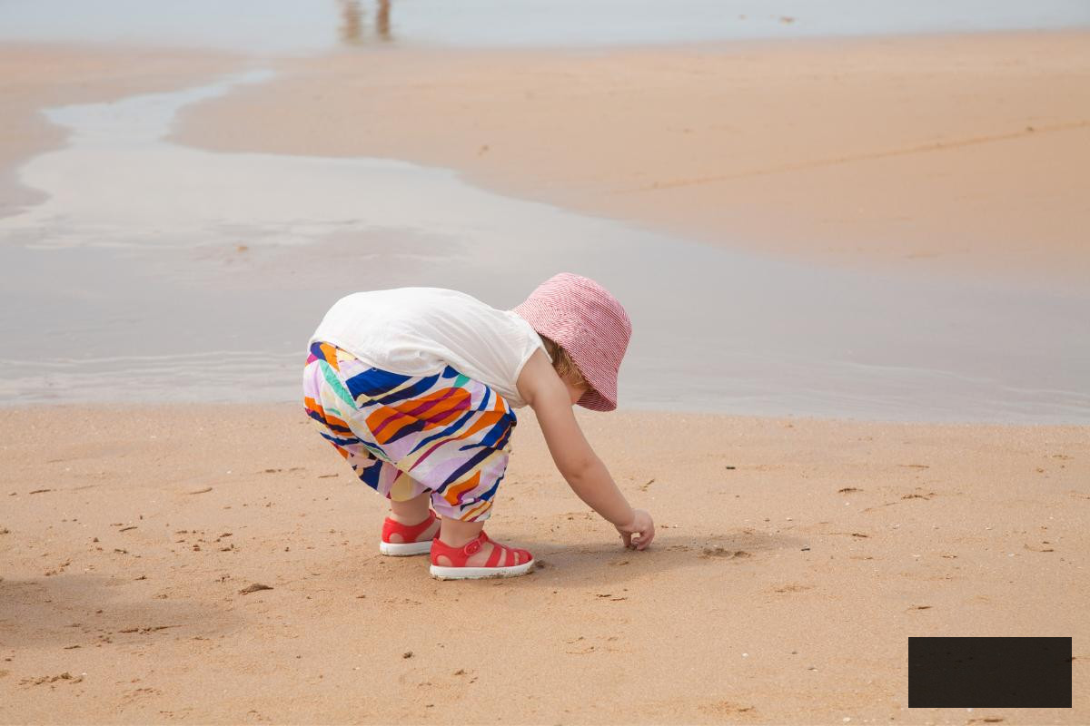 toddler on a beach scavenger hunt looking for shells in the sand.