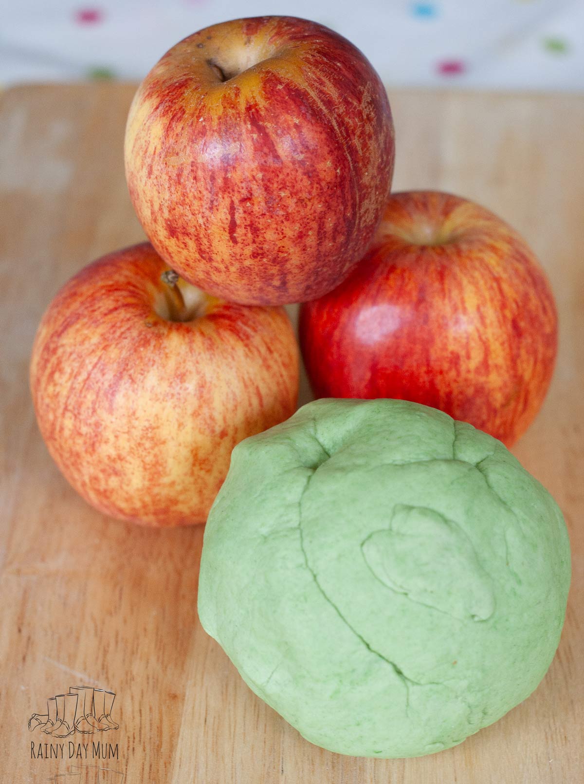 Apples and a ball of playdough on a wooden chopping board.
