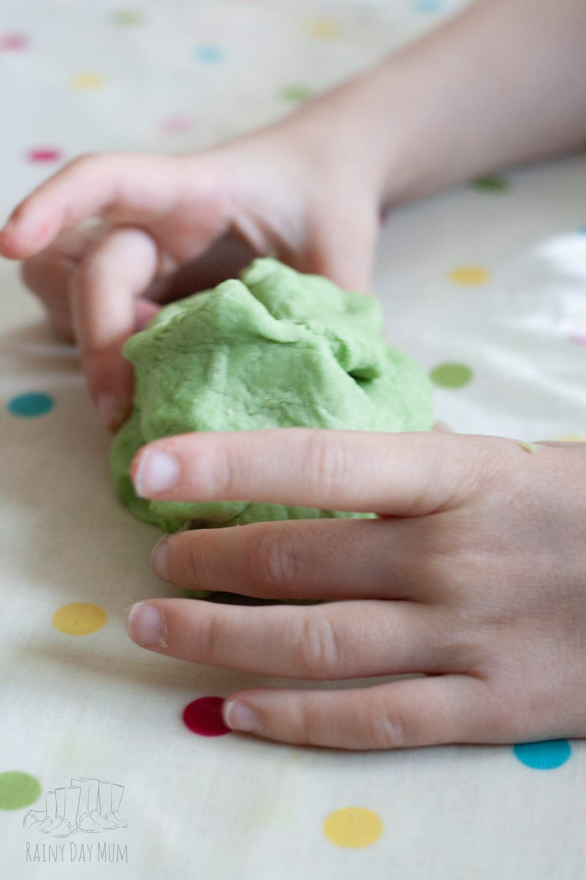 Child engaging with green apple scented playdough on a surface.