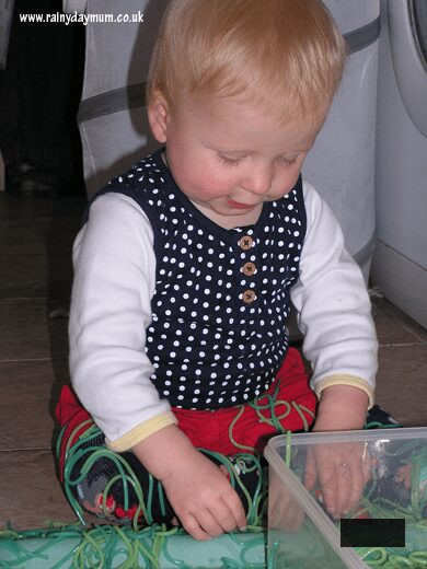 young toddler playing with coloured spaghetti in a sensory bin