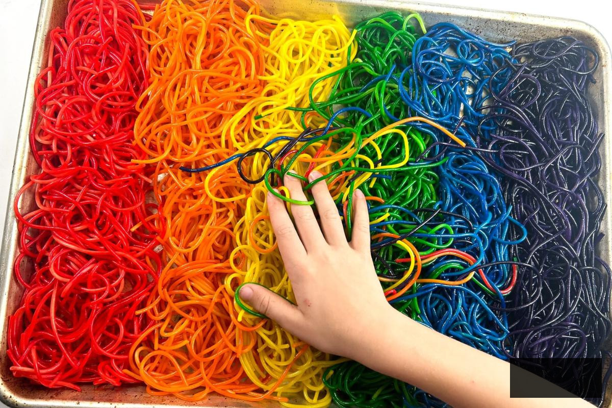 A child playing in a tray of dyed cooked pasta.