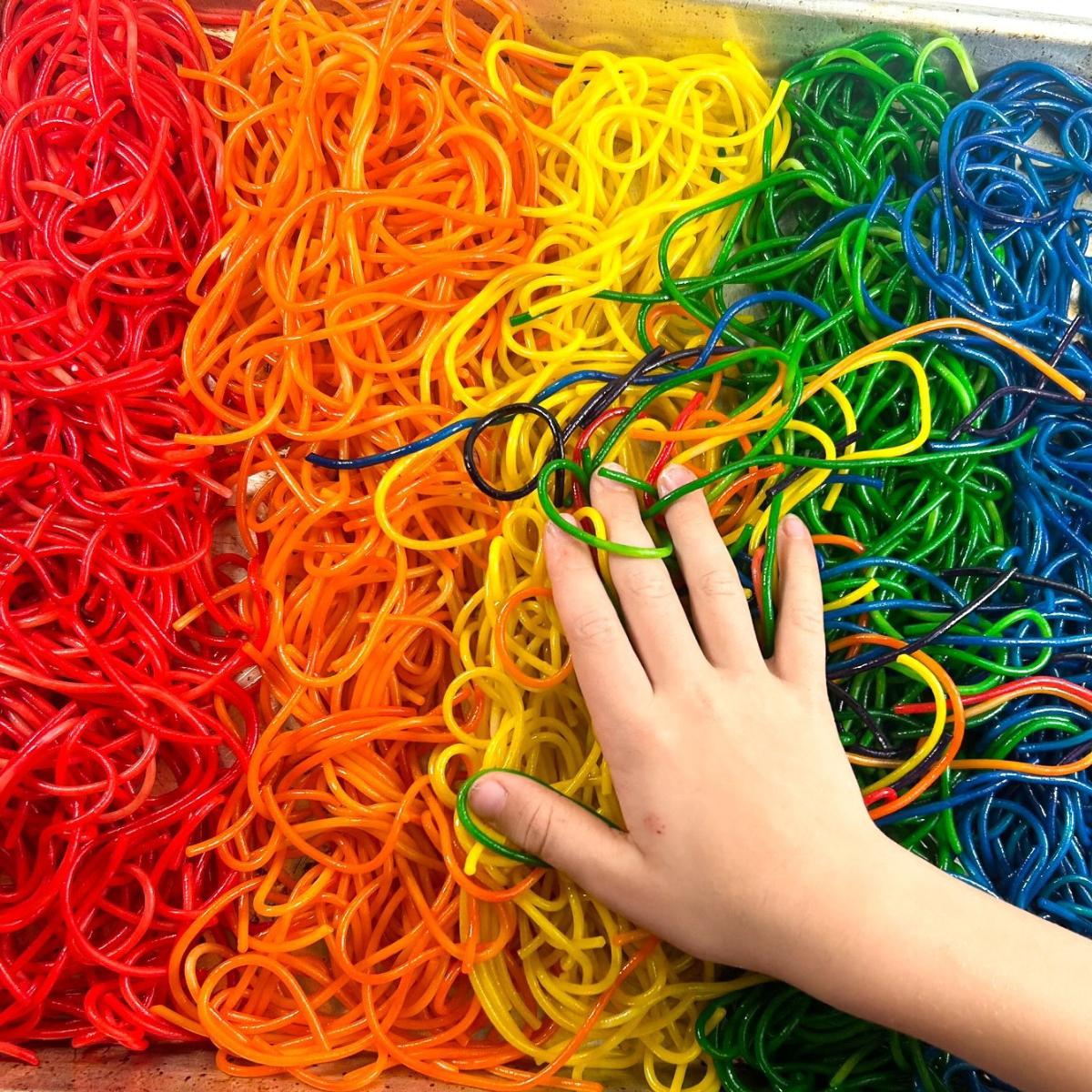 a child engaging with rainbow colored noodles