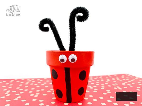 clay pot ladybug craft completed with pipe cleaner antennas on a red spotted paper against a white backdrop