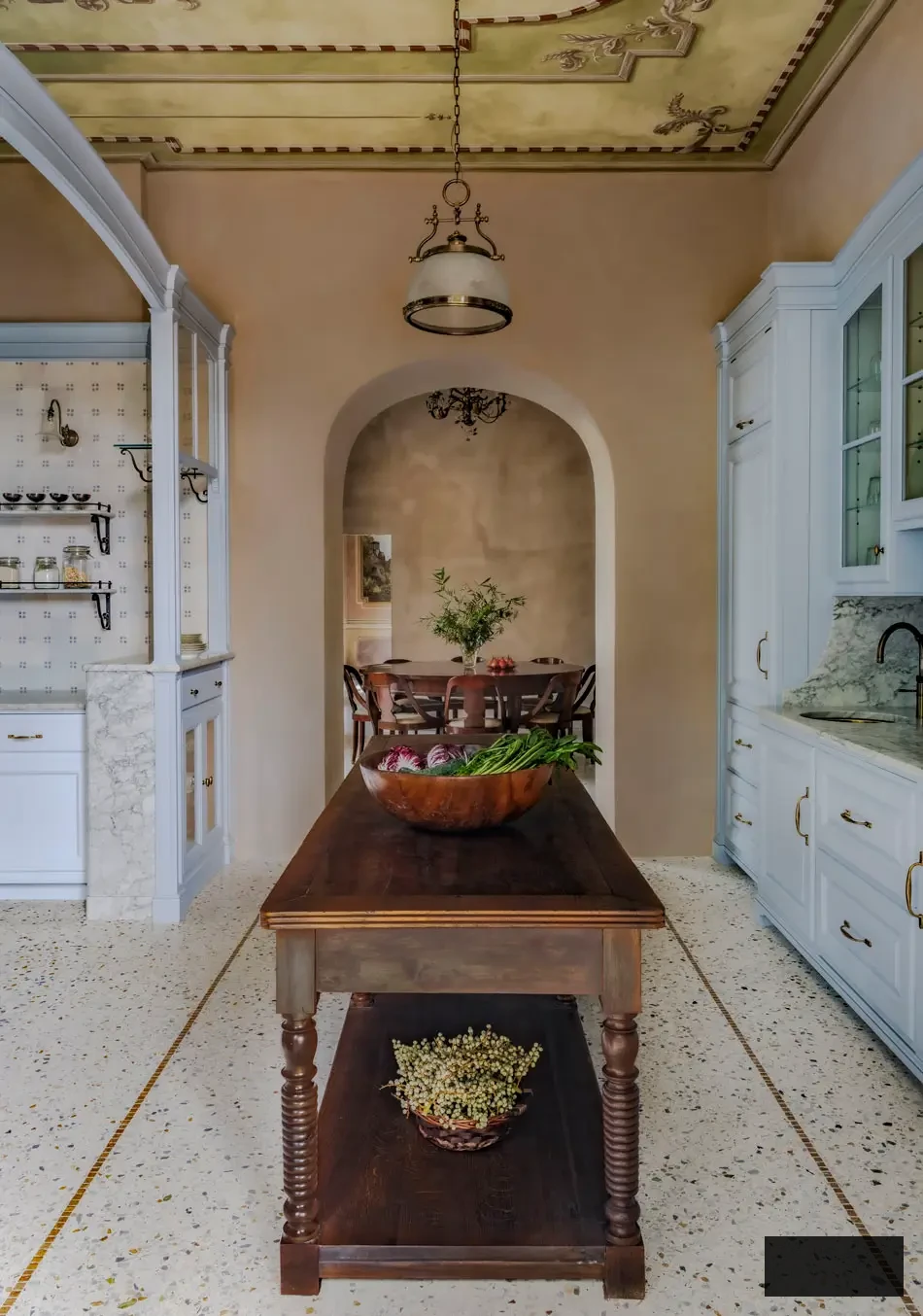 Perspective through the arched entryway from the kitchen to the dining area in an Italian lakeside villa. A sculpted wooden table with turned legs anchors the composition beneath a fresco-adorned ceiling, emphasizing Artichoke’s precise architectural craftsmanship and the harmony of hues and textures throughout.
