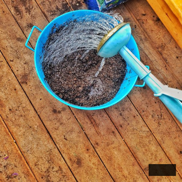 bright blue metal container filled with soil that is being watered