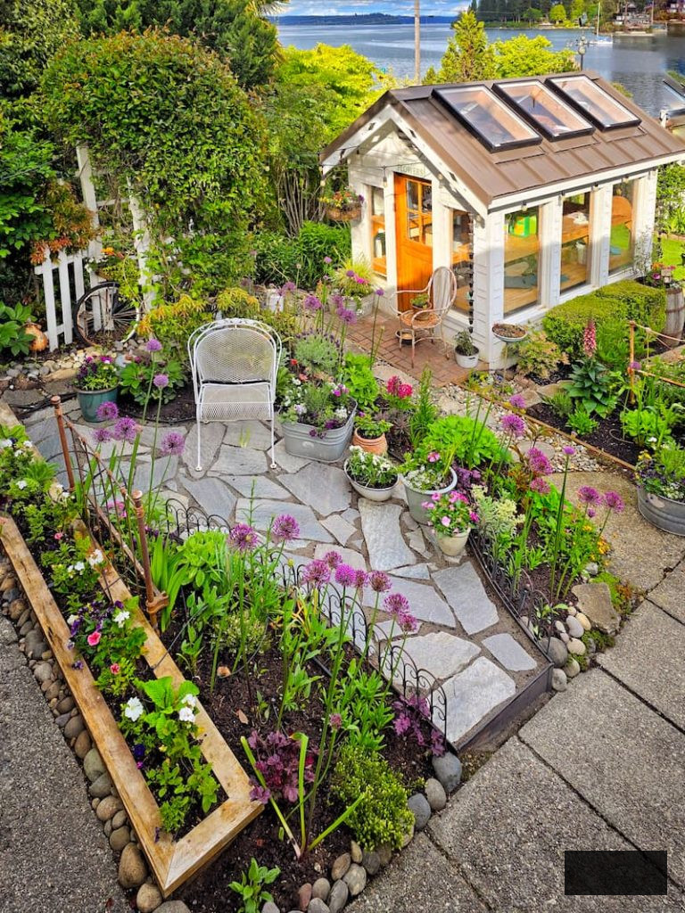 greenhouse and stone patio with flower containers and purple alliums