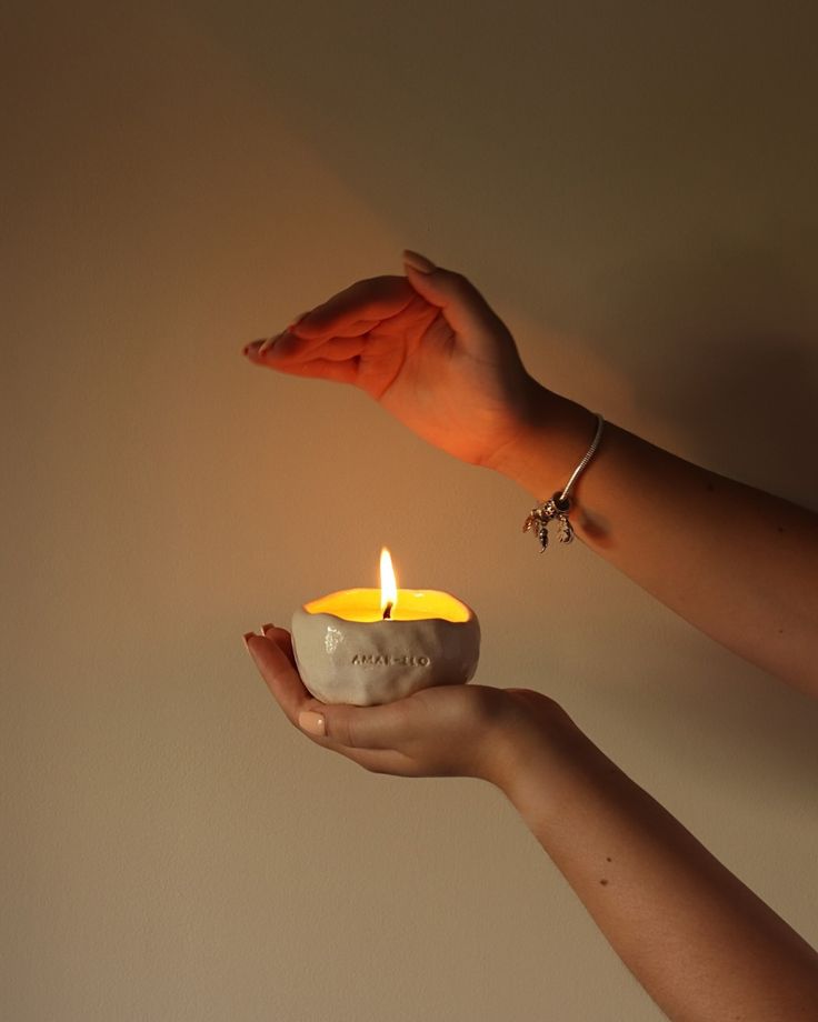 Hands holding a lit handmade candle in a ceramic container