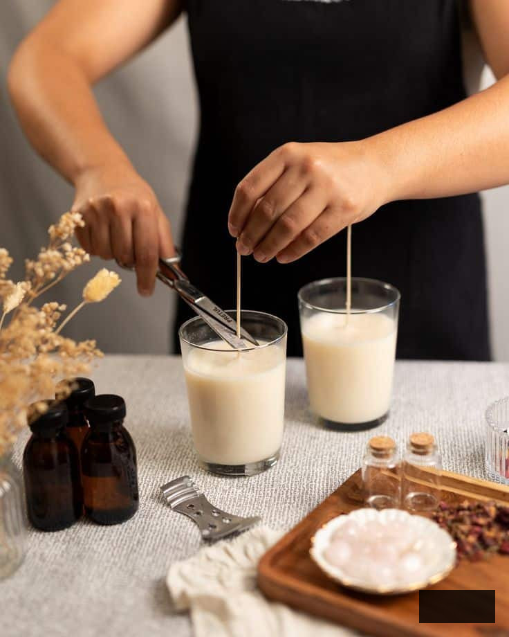 Homemade candle materials featuring glass jars, wicks, essential oils, and wax