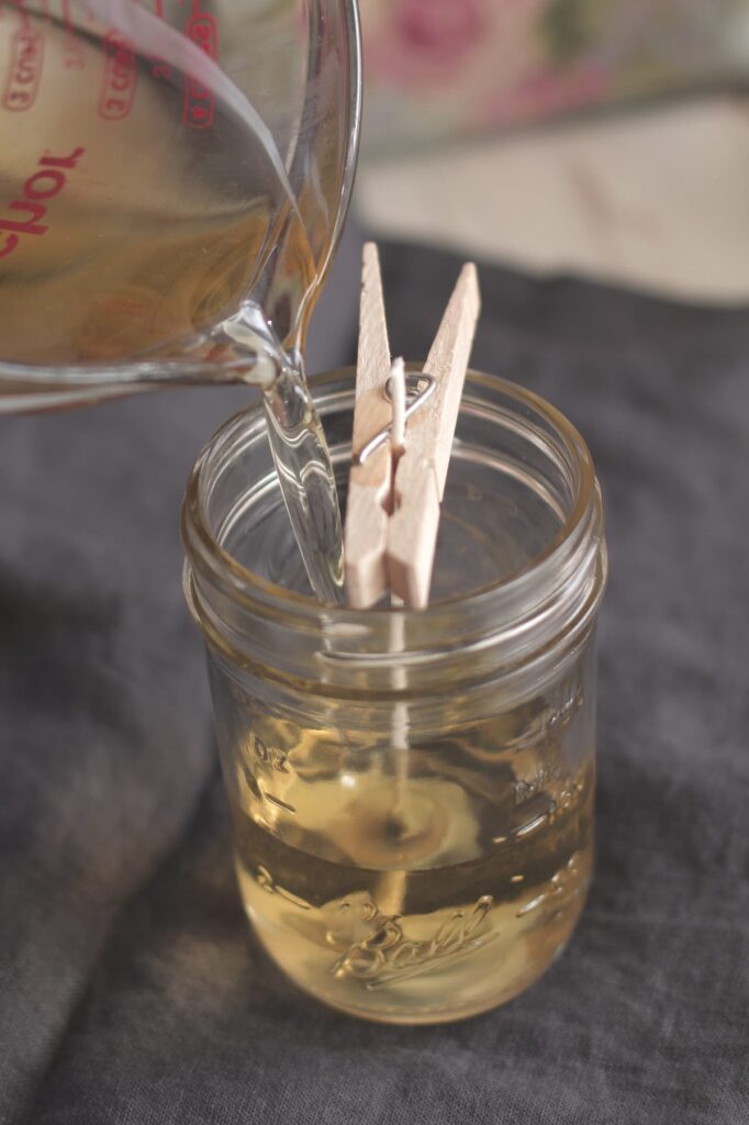 Pouring melted wax into a mason jar with a centered wick for a homemade candle