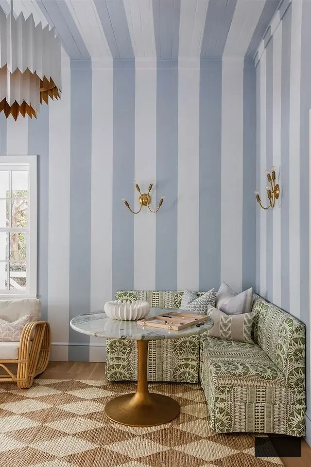Coastal breakfast nook by Megan Molten Interiors featuring light blue striped wallpaper, a built-in banquette, and soft natural textures.