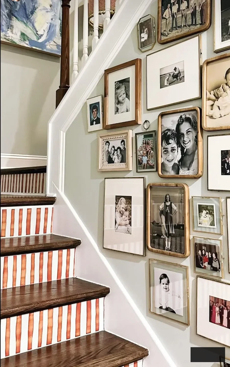 Striped staircase risers beneath a family gallery wall, featuring warm terracotta-and-white stripes that add personality to a traditional hallway.