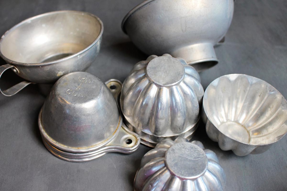 Pilhas de xícaras de medição de alumínio vintage, moldes de gelatina, funis e outros itens de cozinha.
