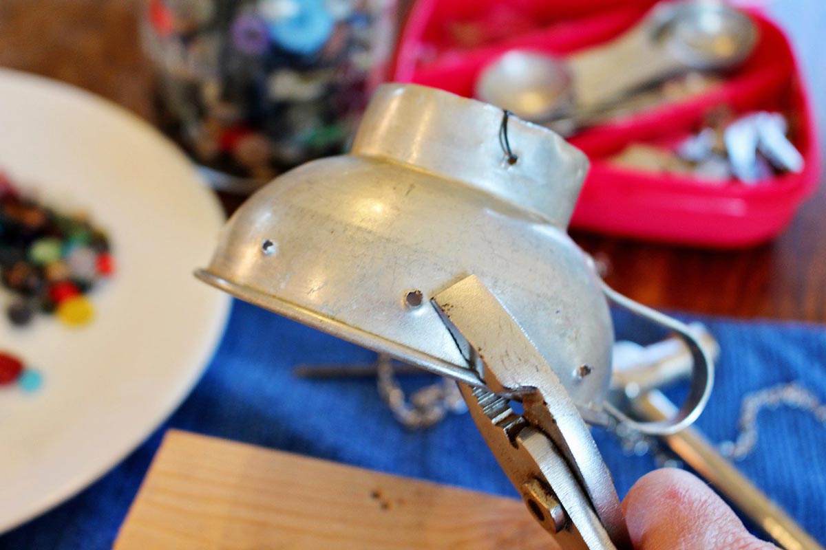 Um funil vintage sendo segurado com um par de alicates, com furos perfurados na lateral.
