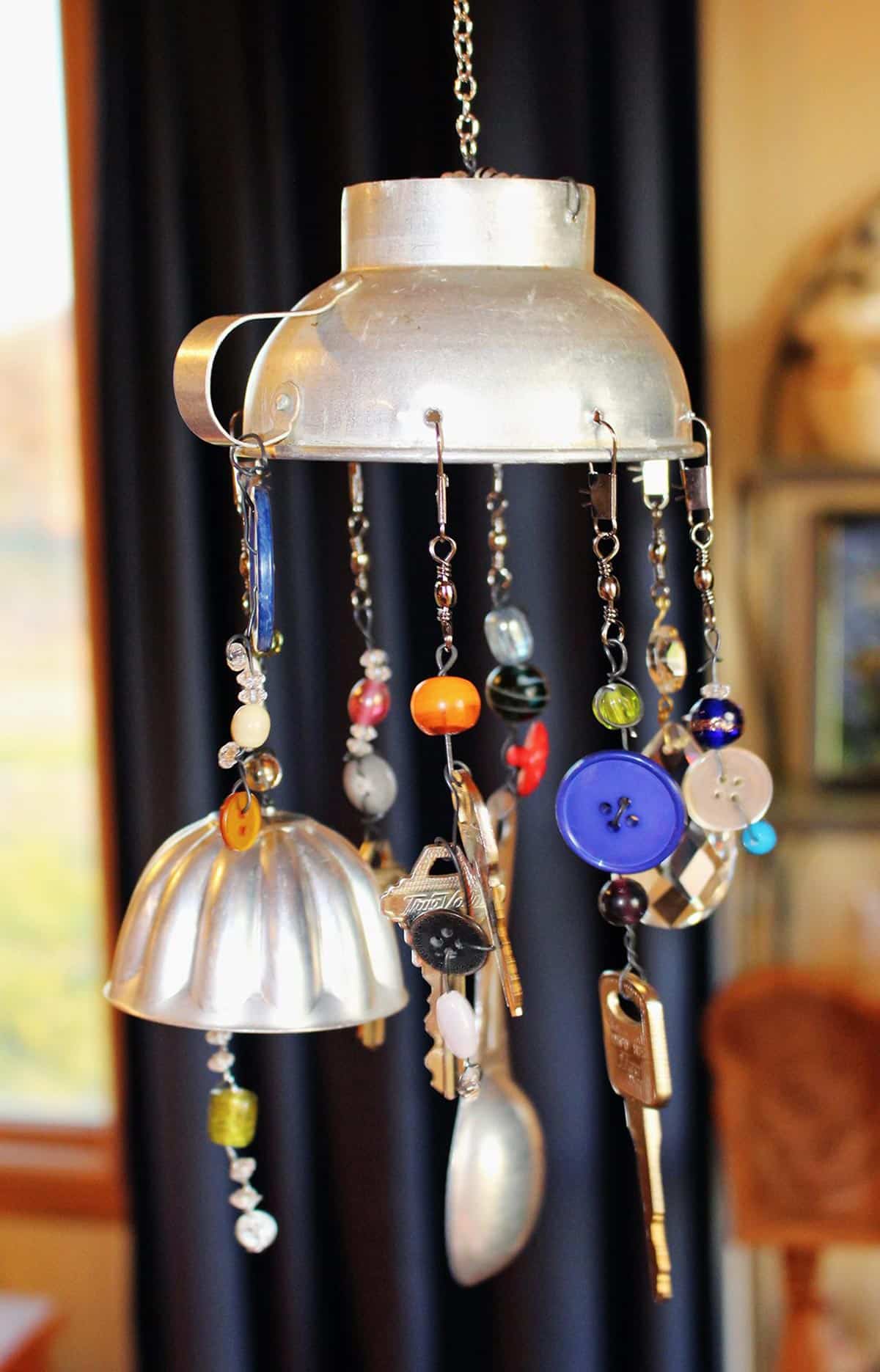 Um sino de vento DIY finalizado feito com contas e itens de cozinha vintage pendurado em um ambiente interno.