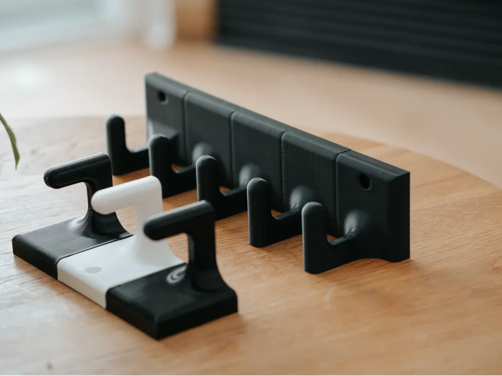 Black and white 3D-printed guitar wall hangers on a wooden table, designed for compact and secure instrument storage.