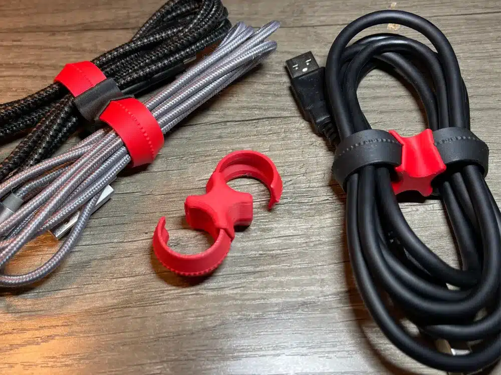 3D printed cable clips organizing red and black charging cables on a wooden desk