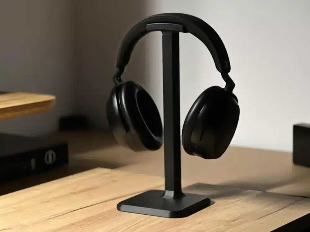 Black over-ear headphones on a stylish stand, situated on a wooden desk, crafting a contemporary and minimalist workspace ambiance.