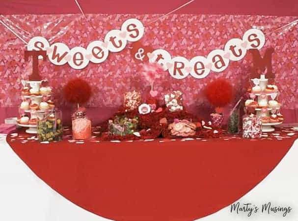 Estas decorações de 25º aniversário são perfeitas para uma cerimônia de renovação de votos fácil e econômica, celebrando 25 anos de casamento juntos! Faixa de doces e guloseimas acima da mesa da recepção de aniversário do Dia dos Namorados