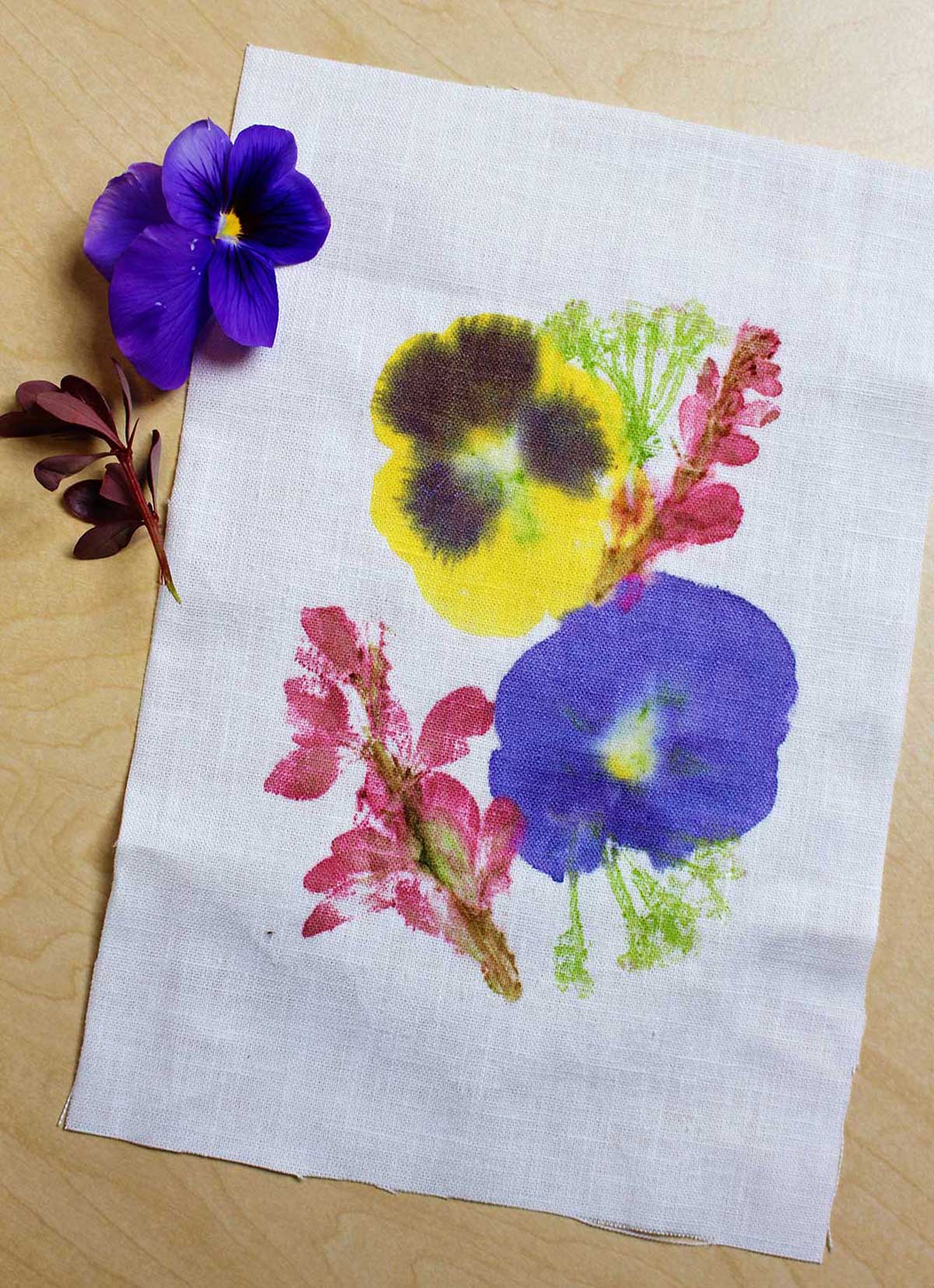Um pedaço de tecido branco com impressões de flores marteladas sobre ele com duas flores descansando ao lado.