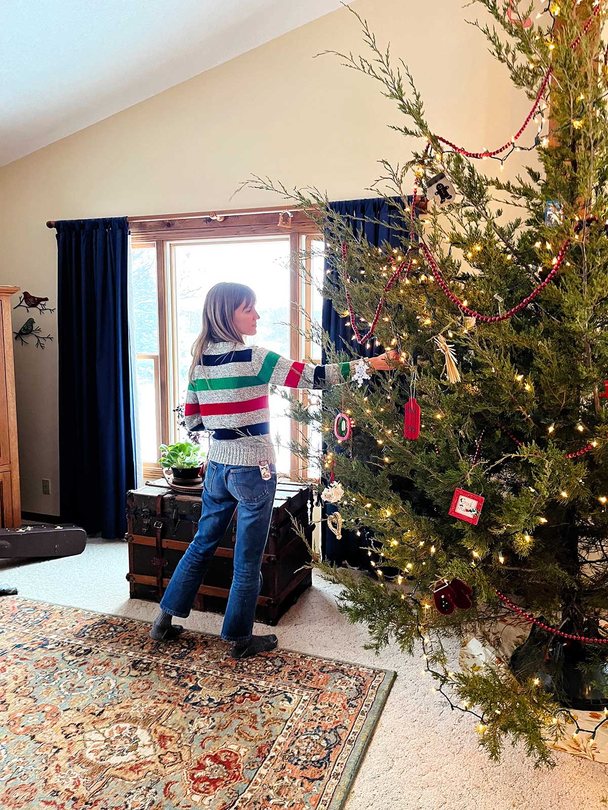 Mulher com suéter listrado pendura ornamento na árvore de Natal.