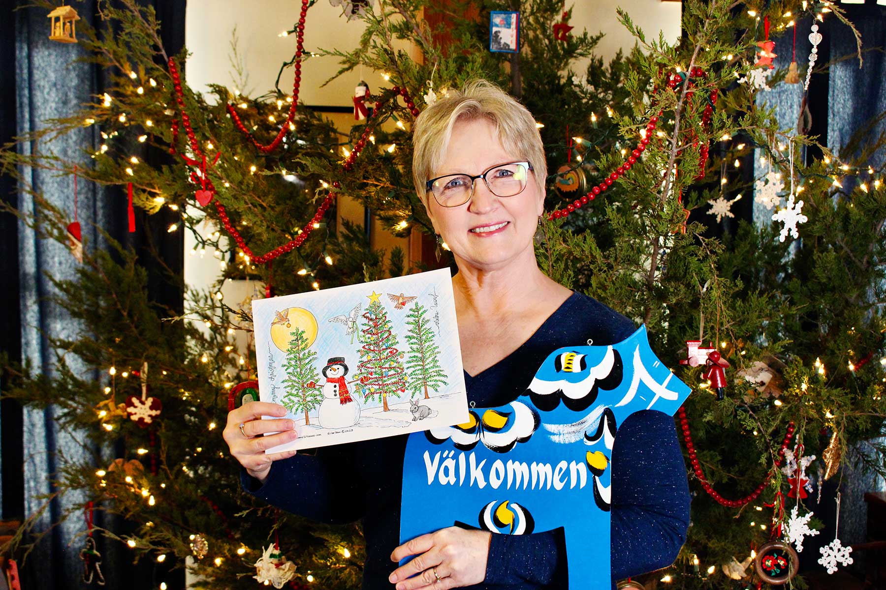 Foto da Nana segurando uma página de colorir de árvore de natal completa em frente à sua árvore de natal.