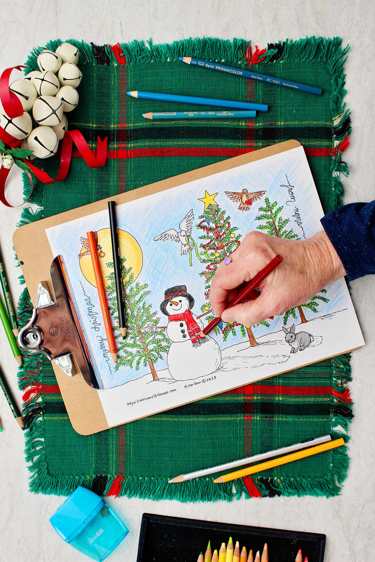 Mão colorindo o cachecol do boneco de neve de vermelho na página para colorir da árvore de natal.