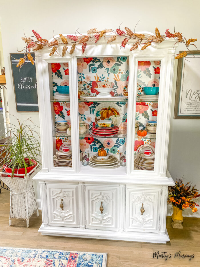 Aparador branco com papel de parede floral e decoração de outono dentro