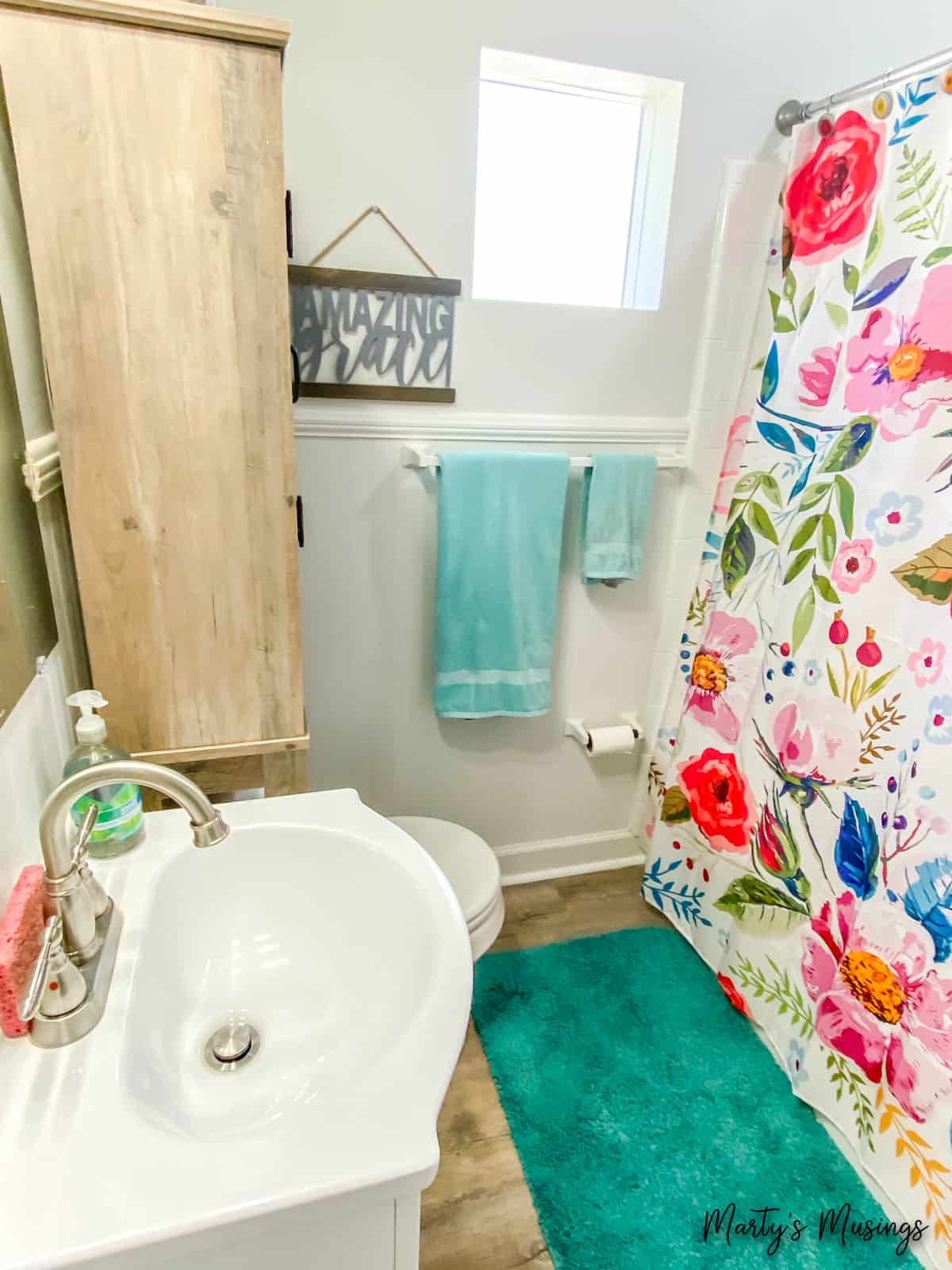 Pequeno banheiro com cortina de chuveiro floral e toalhas aqua