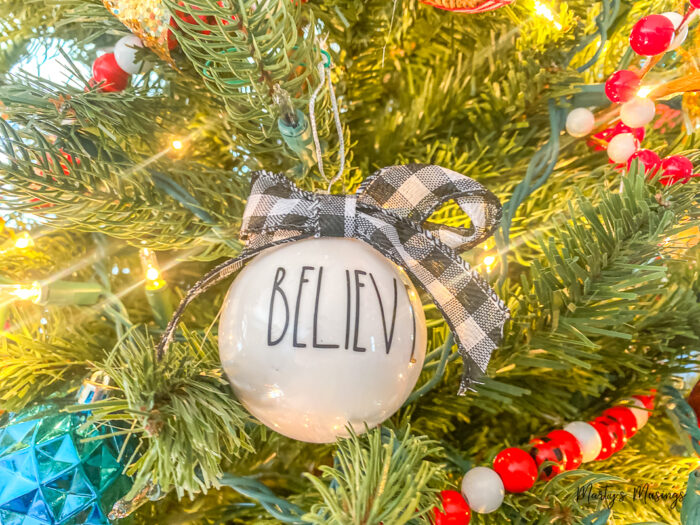 Ornamento branco com a palavra believe na árvore de Natal