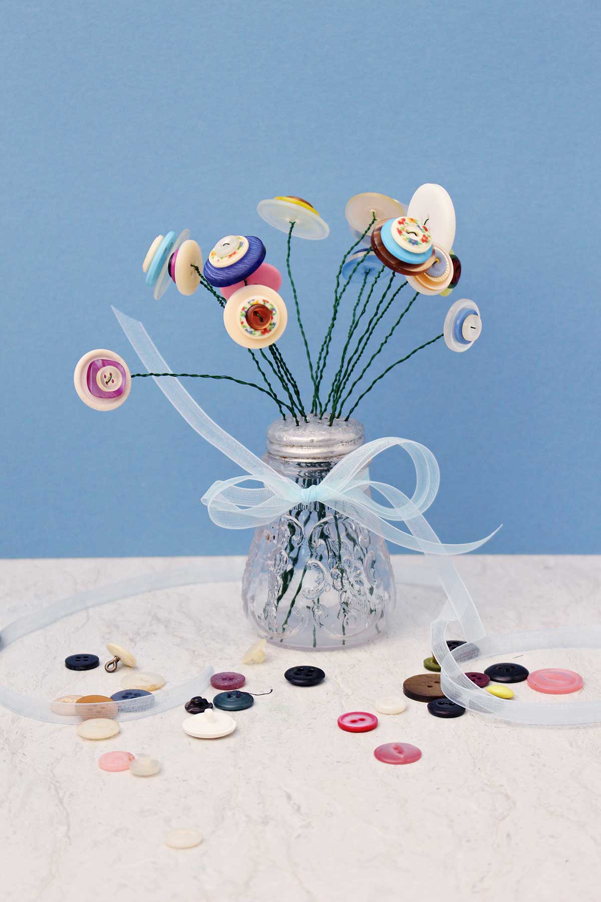 um saleiro cheio de flores de botão com uma fita amarrada ao redor, contra um fundo azul.