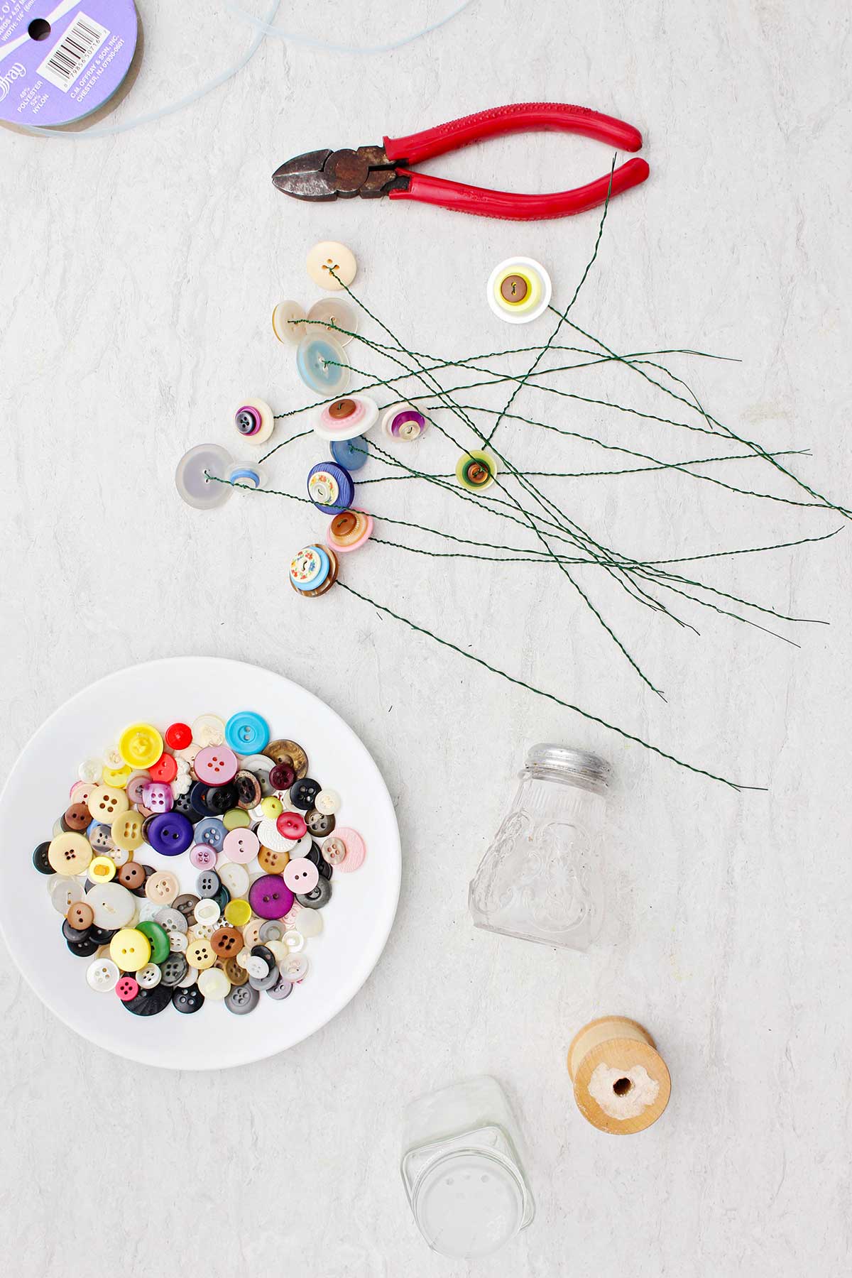 Cauzas de flores de botão, cortadores de fios, um prato de botões coloridos e saleiros de vidro.