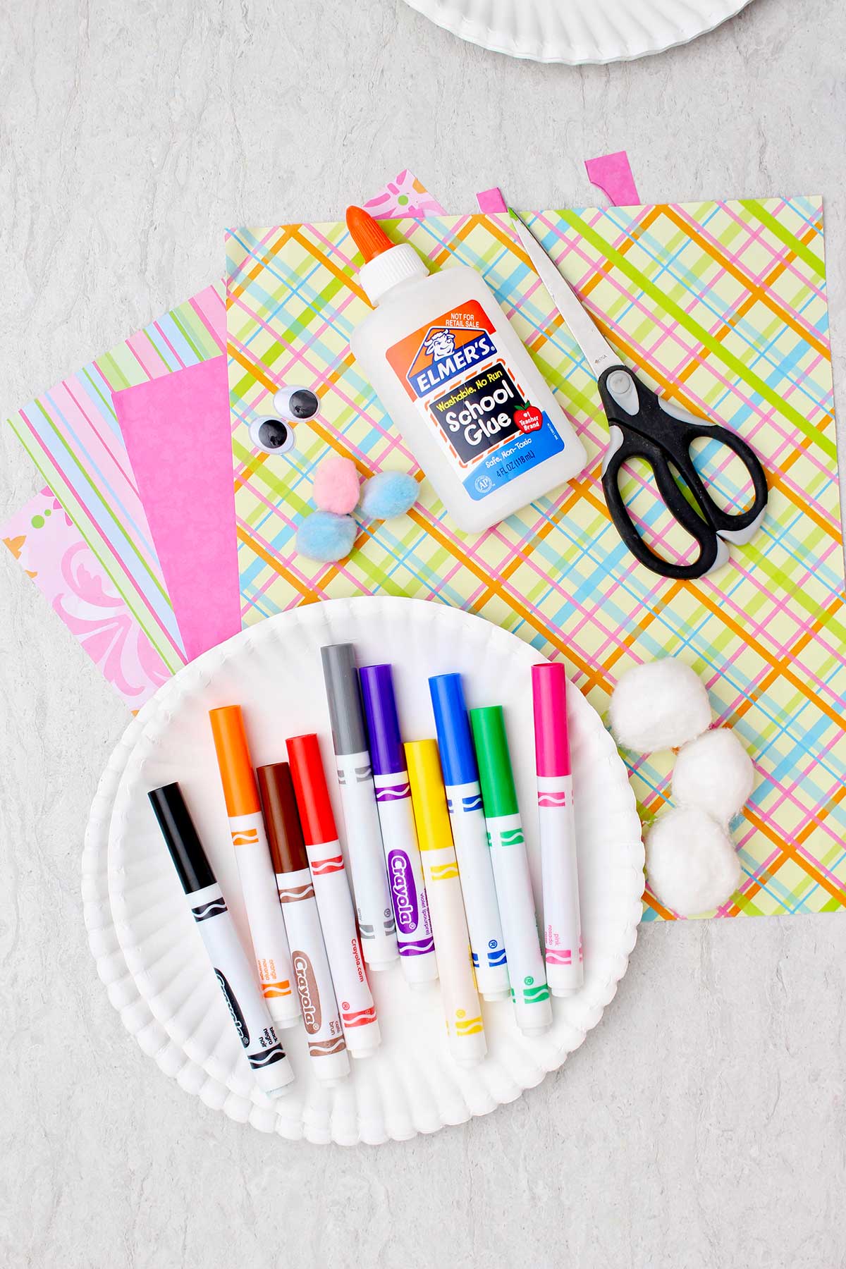 Um prato com marcadores, tesoura, cola, papel de scrapbook, olhos móveis e bolas de algodão.