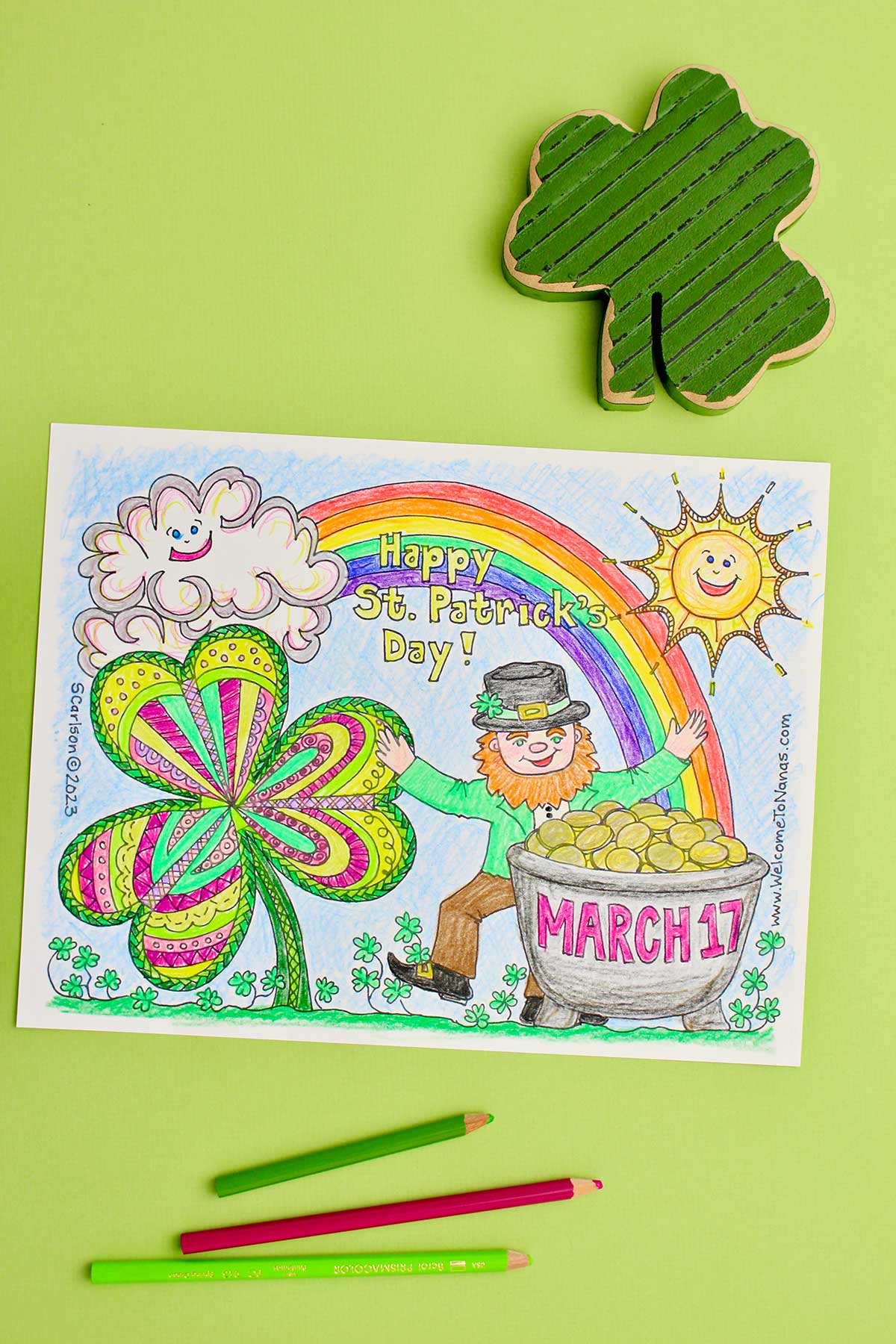 Imagem vertical da folha de colorir do Dia de São Patrício completa contra um fundo verde limão com três lápis de cor e um trevo de madeira próximos.