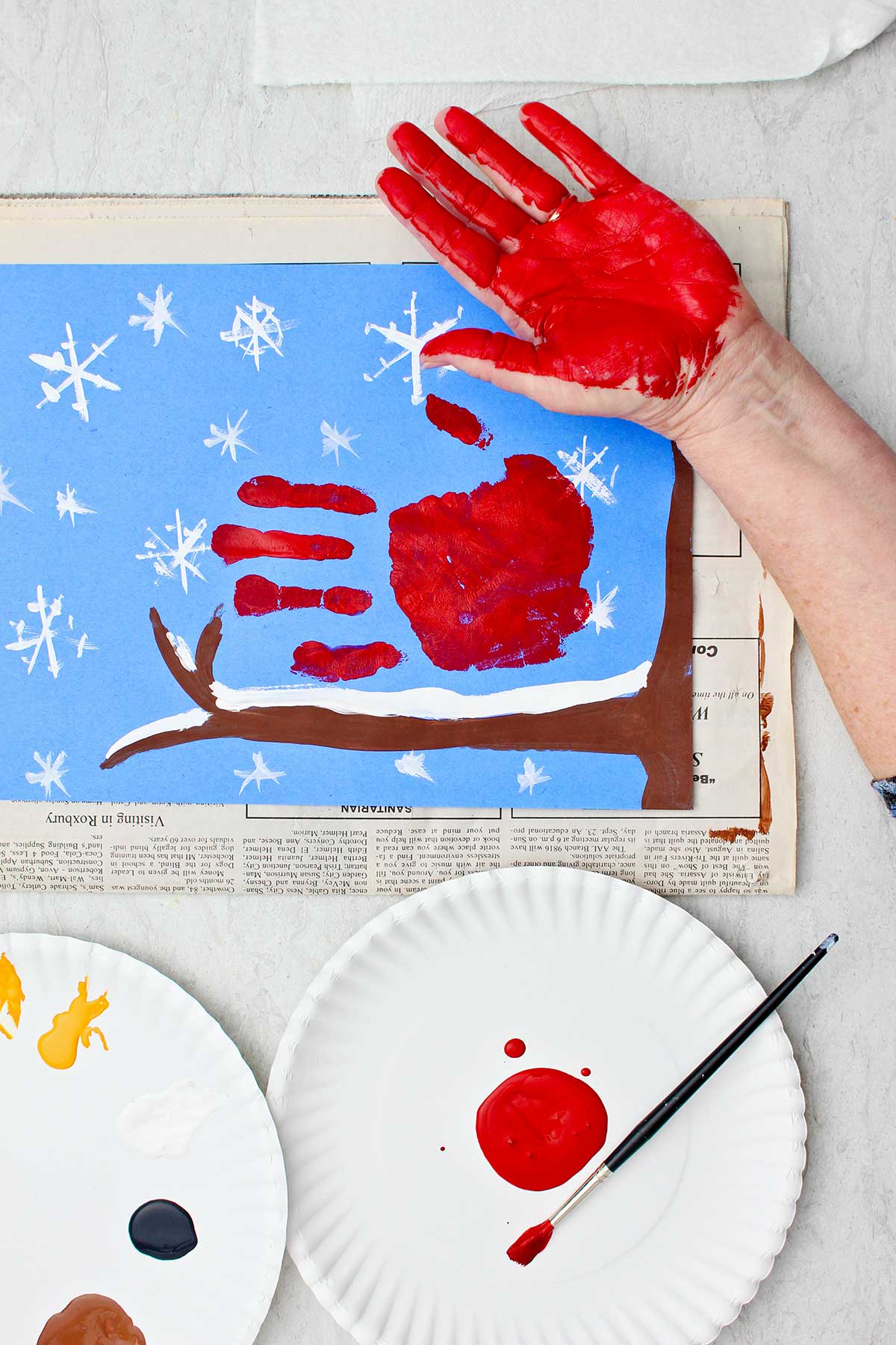 Pessoa mostrando a mão pintada de vermelho após carimbá-la em seu papel de construção de cena de inverno.