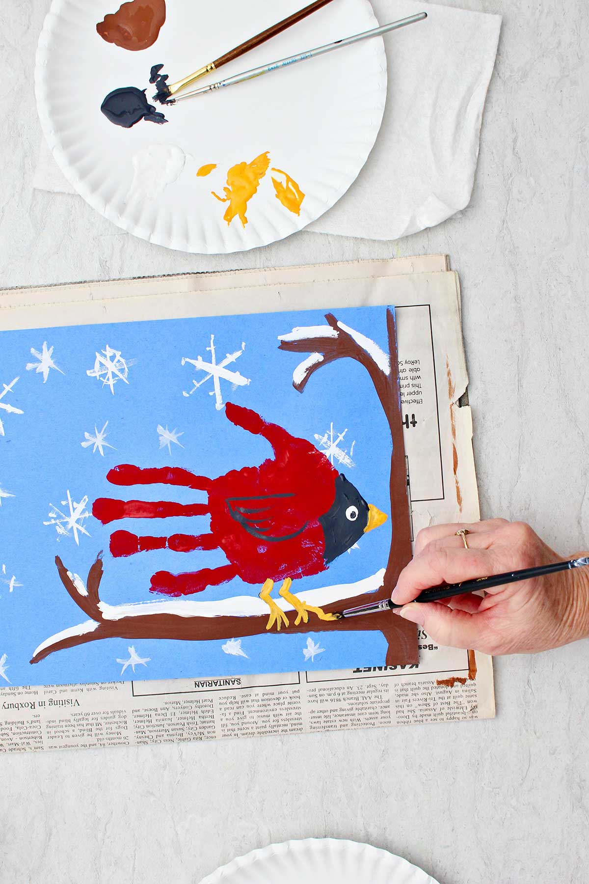 Pessoa pintando os detalhes finais em uma pintura de mão de cardeal sentada em um galho coberto de neve.