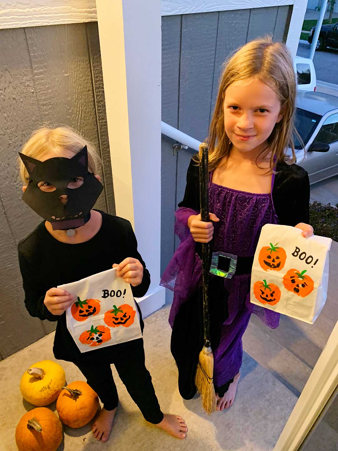 Duas meninas jovens, vestidas de gato preto e bruxa, fazendo trick or treating.