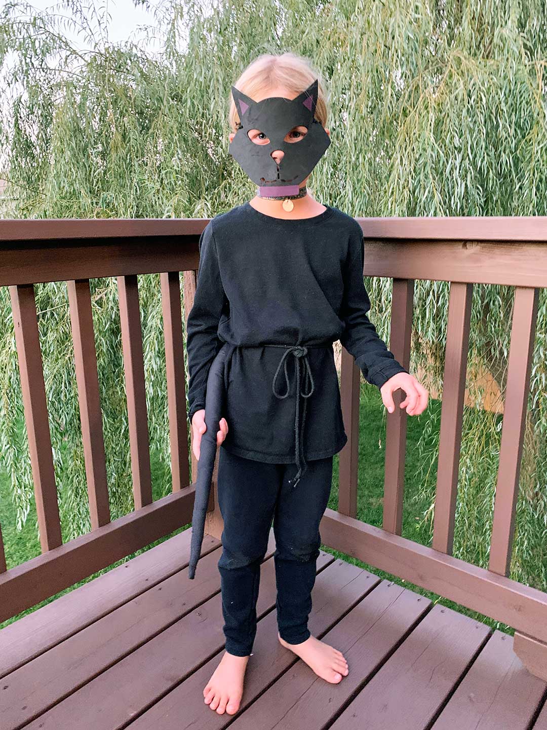 Uma garota jovem com cabelo loiro vestida como um gato preto em um deck.