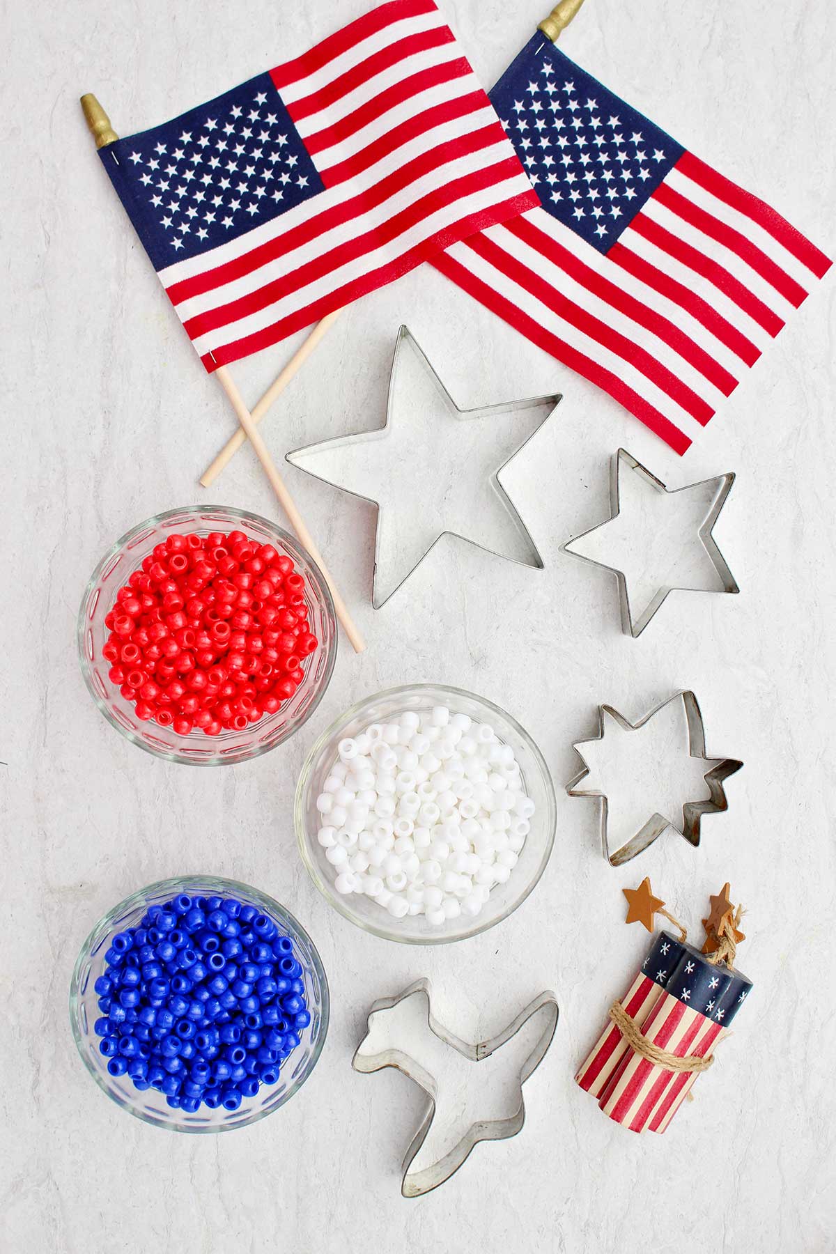 Três tigelas com pérolas vermelhas, brancas e azuis, cortadores de biscoito e decorações da bandeira americana.