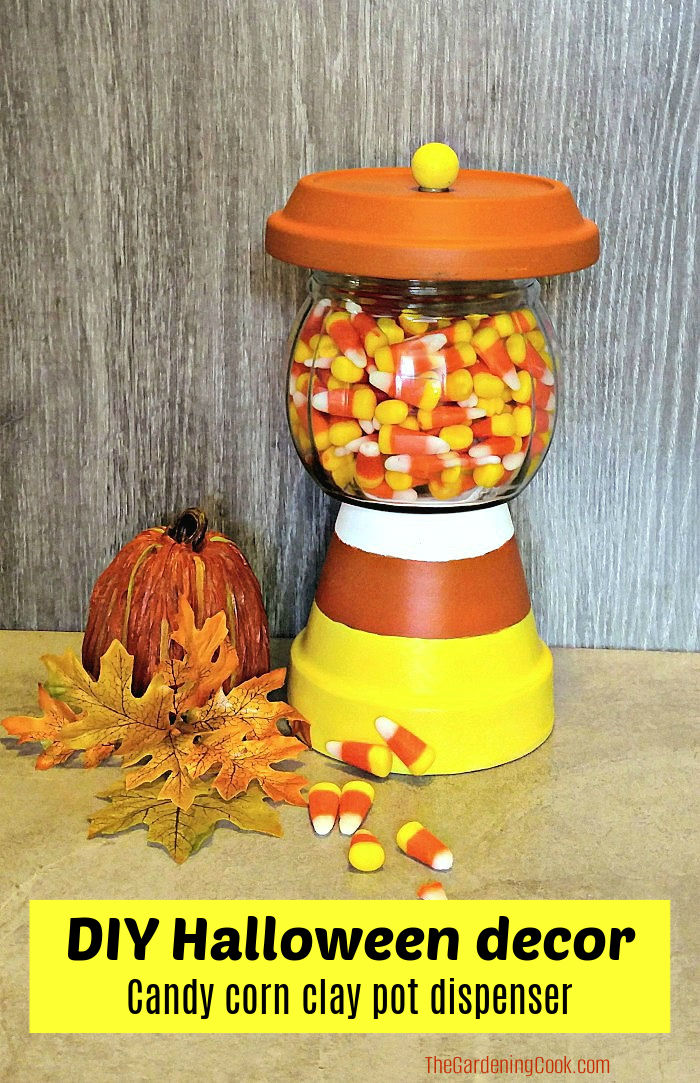 Um vaso de terracota pintado, saucer e jarro de vidro feitos em um pote de doces de Halloween. A caixa de texto amarela diz decoração DIY de Halloween - dispensador de pote de barro de doces de milho