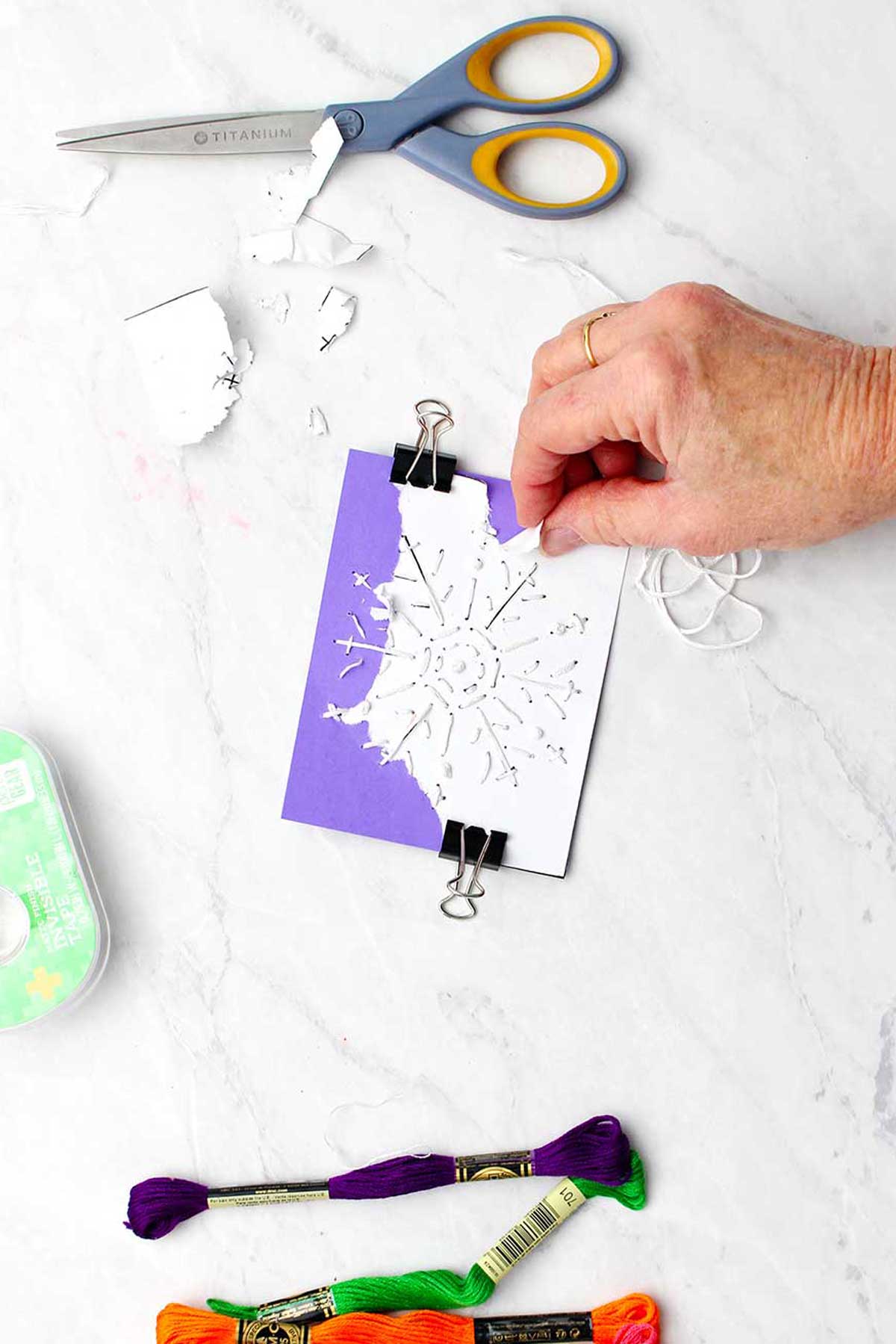 Mão rasgando o template de floco de neve de papel branco do cartão roxo.