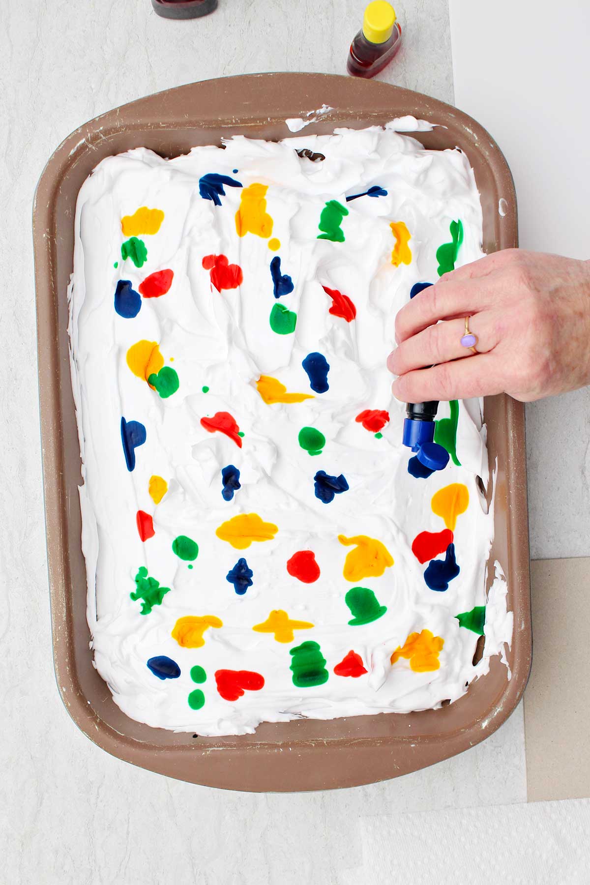 Pessoa borrifando gotas de corante alimentar em uma panela de creme de barbear alisado.