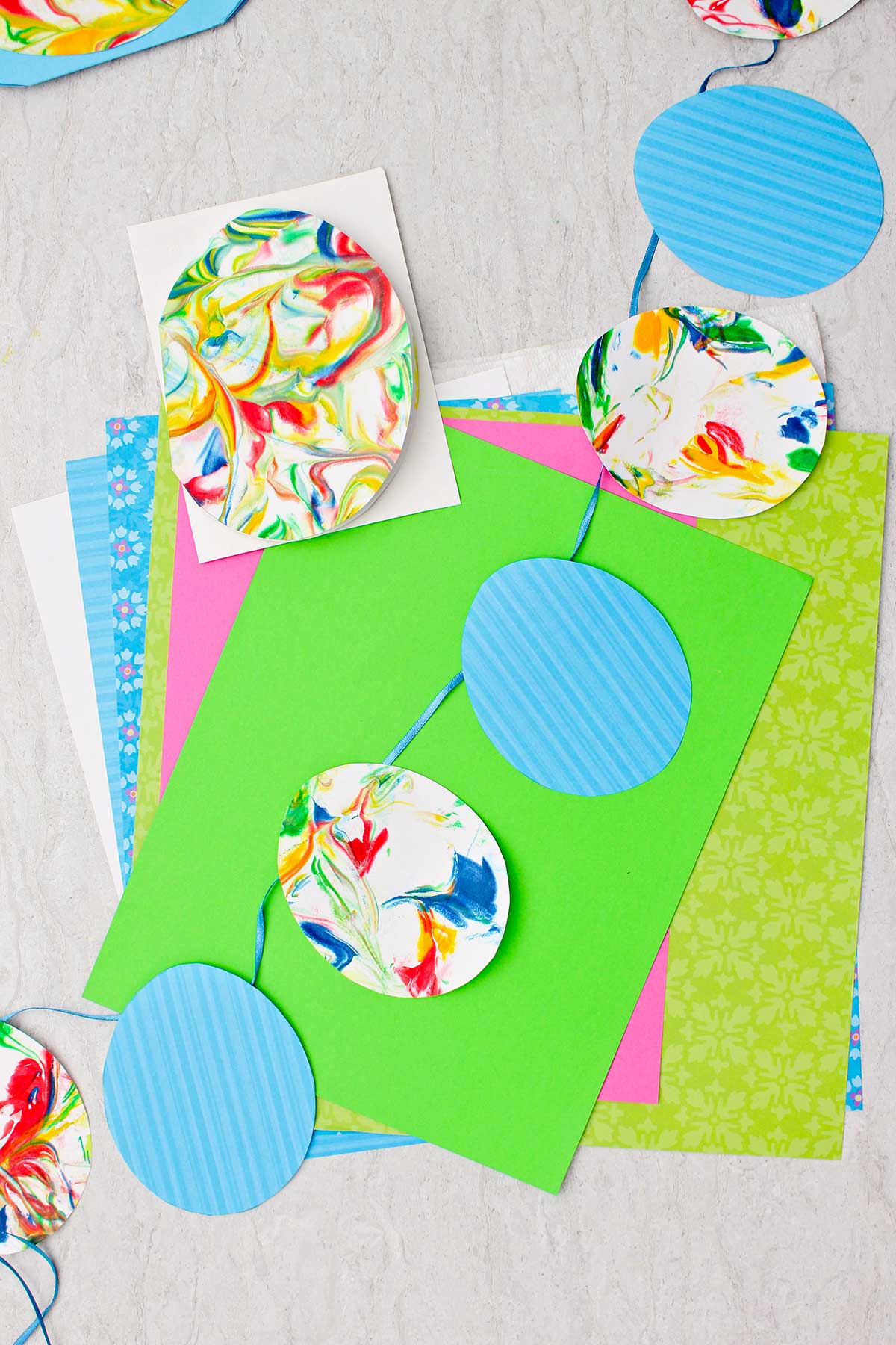Bandeira de ovo de Páscoa feita com ovos de papel listrado azul e ovos de papel mármore em uma fita azul com outros pedaços de papel colorido próximos.