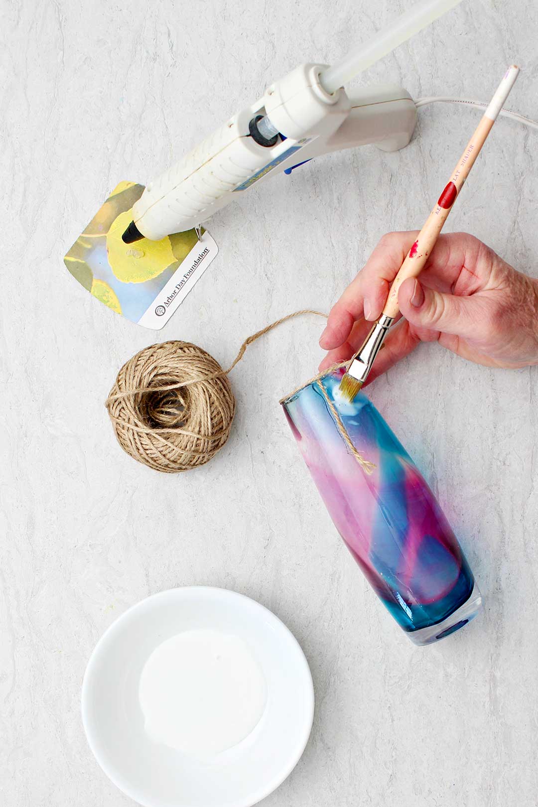 Pintando à mão cola branca no vaso de vidro com um pequeno pedaço de corda preso.