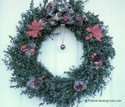 Guirlanda de Natal de Buxo com sino e decorações em uma porta branca.