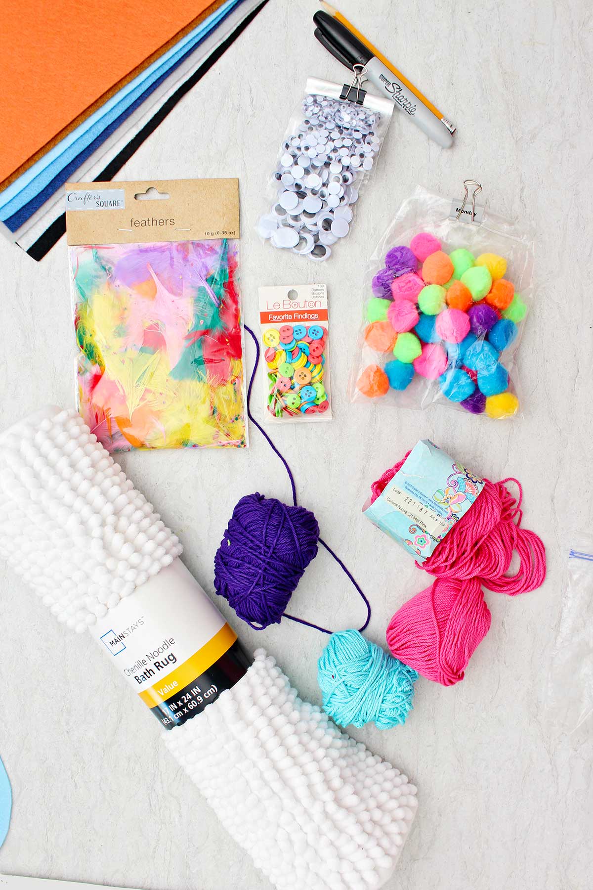 Itens para fazer fantasias de Halloween DIY. Olhos de inseto, penas, pompons, cordão colorido, botões e um tapete de banho branco.