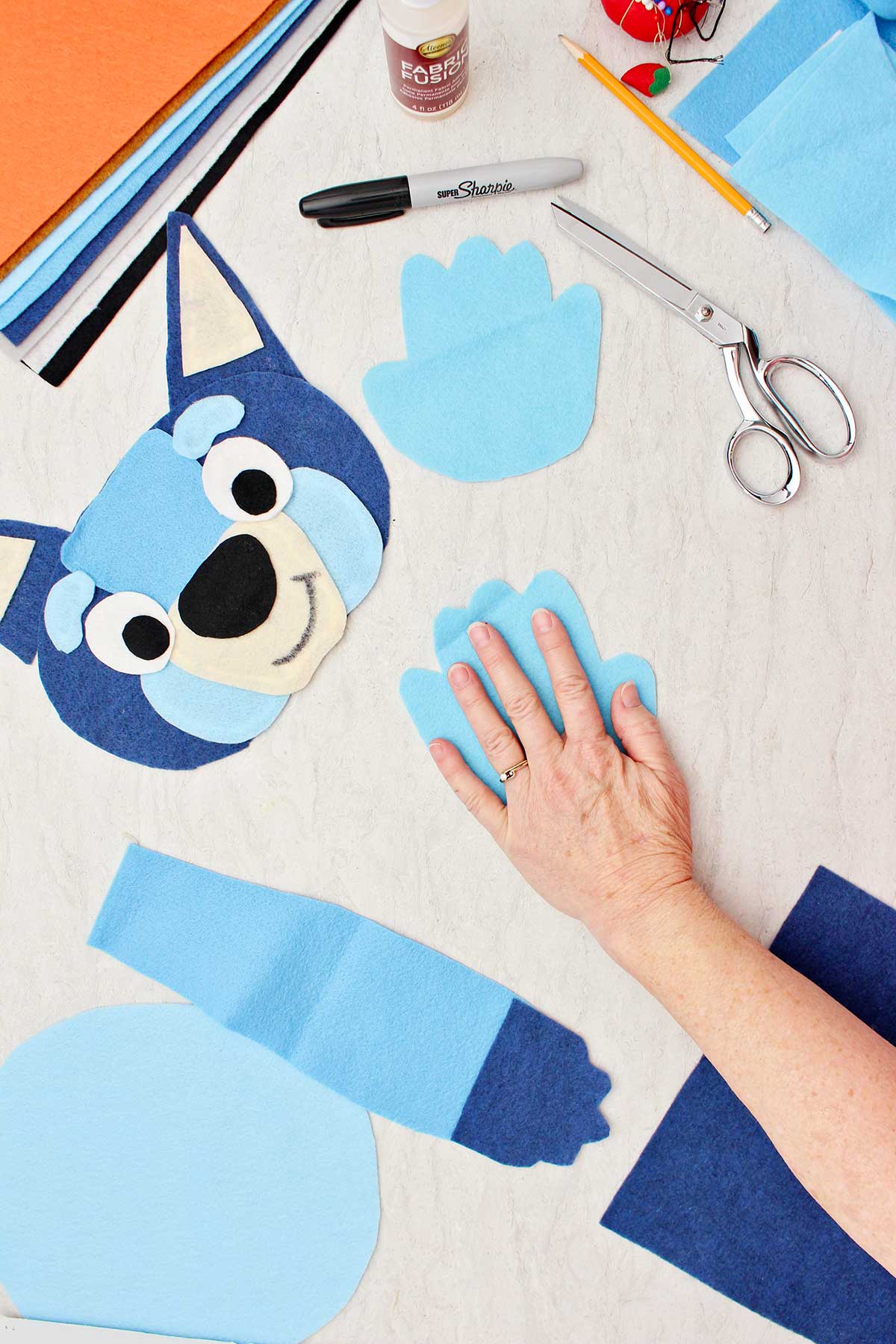 Pessoa medindo sua mão para fazer uma pata azul para a fantasia do Bluey com outras peças da fantasia ao redor.